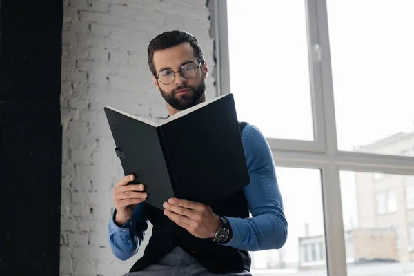 Homme d'affaires barbu à la mode lecture carnet — Photo de stock