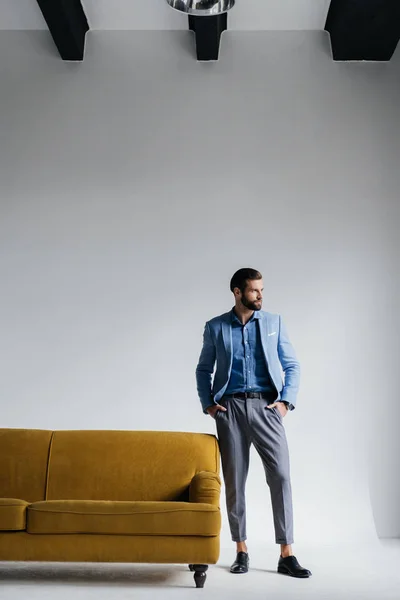 Homem elegante em terno azul posando no sofá amarelo — Fotografia de Stock
