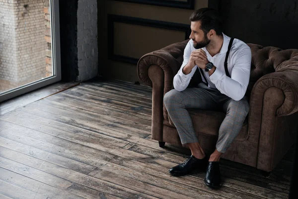 Schöner, stylischer Mann sitzt im Sessel und schaut auf Fenster, Loft-Interieur — Stockfoto