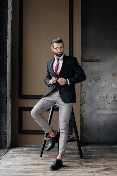 Schöner stylischer Geschäftsmann im Anzug posiert auf einem Hocker im Loft-Interieur — Stockfoto