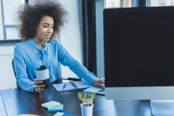 Afrikanisch-amerikanische Geschäftsfrau hält Tasse Kaffee in der Hand und benutzt Laptop im Büro — Stockfoto