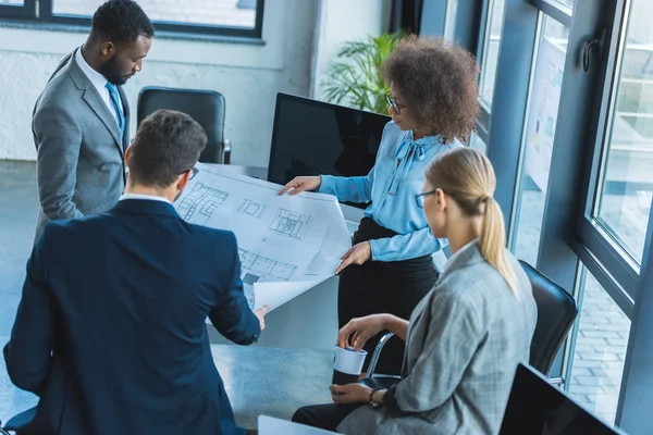 High angle view of multicultural businesspeople looking at blueprint in office — Stock Photo