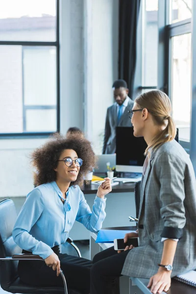 Souriantes femmes d'affaires multiculturelles parlant au bureau — Photo de stock