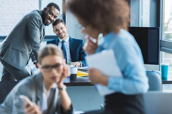 Uomini d'affari multietnici sorridenti che guardano le donne d'affari in carica — Foto stock