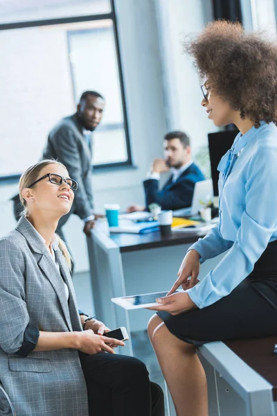 Empresarias multiculturales hablando y mirándose en la oficina - foto de stock