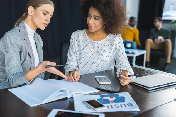 Empresarias multiculturales hablando de documentos en el cargo - foto de stock