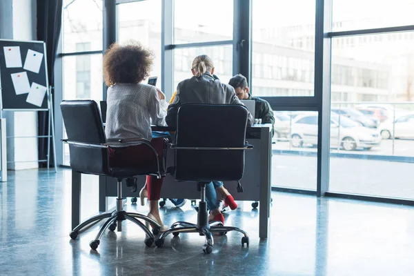 Vue arrière des gens d'affaires multiculturels assis à table dans l'espace de travail — Photo de stock