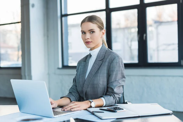 Beautiful businesswoman using laptop in office and looking at camera — Stock Photo