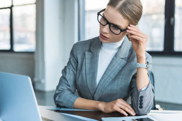 Femme d'affaires dans des lunettes à la recherche d'un ordinateur portable au bureau — Photo de stock