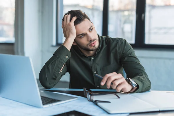 Hombre de negocios guapo sentado en la mesa en la oficina y mirando hacia otro lado - foto de stock