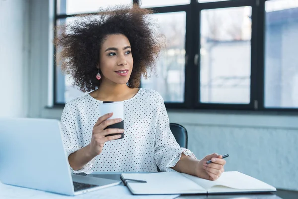 Heureuse femme d'affaires afro-américaine tenant une tasse de café au bureau — Photo de stock