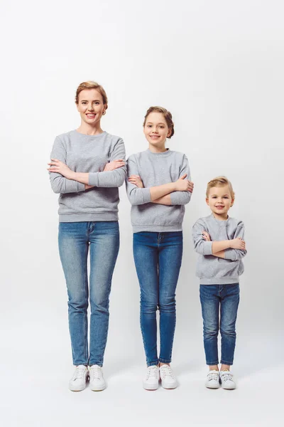 Smiling mother and daughters of different generations in similar clothing with arms crossed isolated on grey — Stock Photo