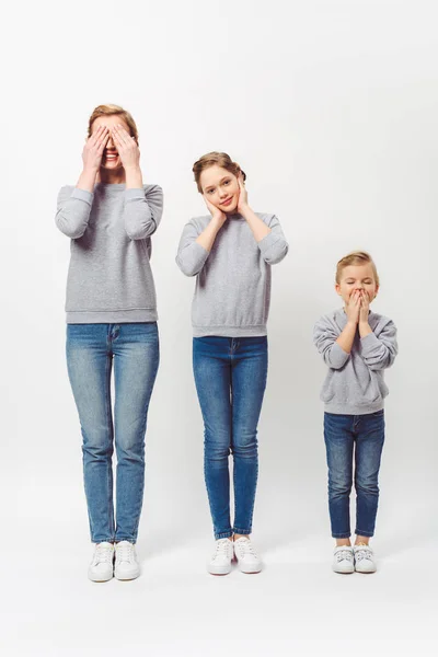 Mother and daughters of different generations in similar clothing covering parts of faces isolated on grey — Stock Photo