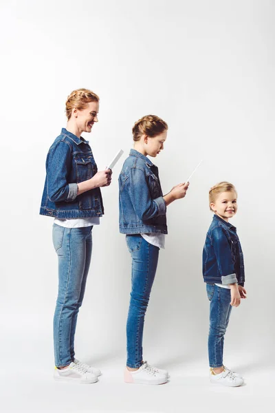 Seitenansicht einer Familie mit Tabletten und kleinem Kind in ähnlicher Jeanskleidung isoliert auf grau — Stockfoto