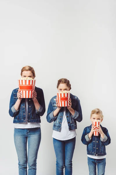 Obscured view of family in similar denim clothing covering faces with popcorn isolated on grey — Stock Photo