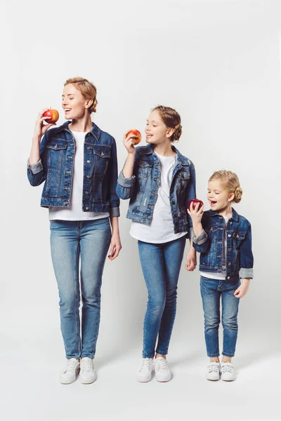 Smiling mother and daughters of different generations in similar clothing with fresh apples isolated on grey — Stock Photo