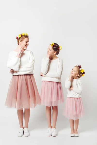 Beautiful mother and daughters in similar clothing with floral wreathes on heads isolated on grey — Stock Photo