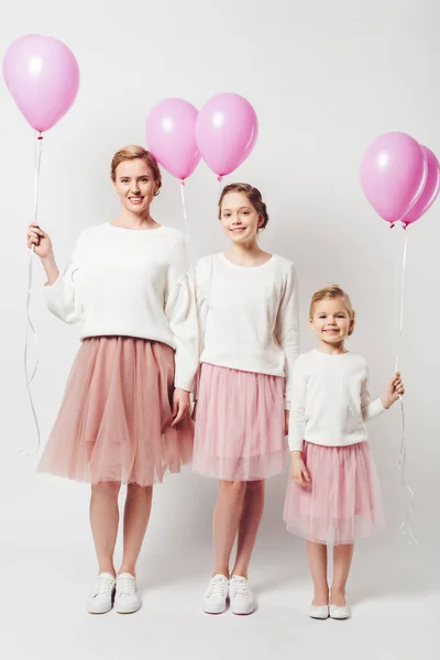 Sonrientes madre e hija en ropa similar con globos rosados aislados en gris - foto de stock