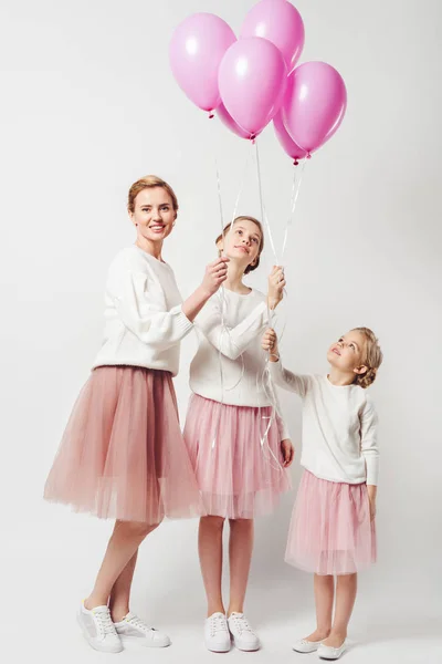 Sonrientes madre e hija en ropa similar con globos rosados aislados en gris - foto de stock