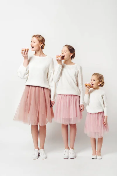 Family in similar clothing eating sweet doughnuts isolated on grey — Stock Photo