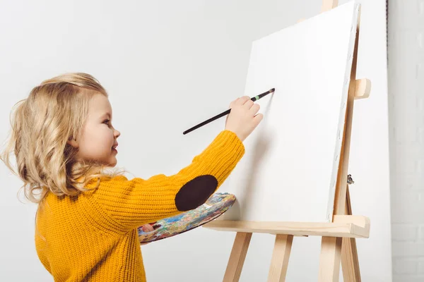 Happy little child painting on canvas with oil paint on white — Stock Photo