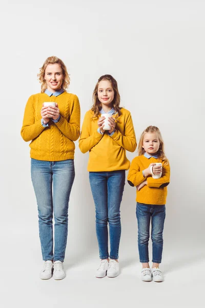 Mother and daughters holding cups of hot hoffee on white — Stock Photo