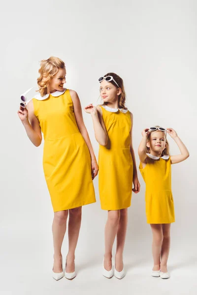 Stylish mother and daughters in similar retro style yellow dresses on white — Stock Photo