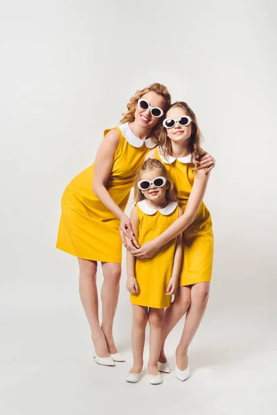Embracing mother and daughters in similar retro style yellow dresses on white — Stock Photo