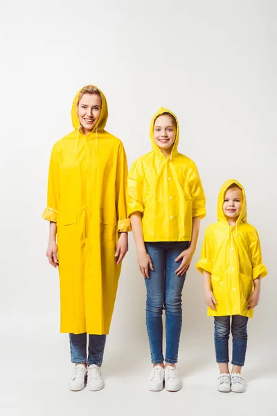 Feliz madre e hijas en impermeables amarillos de pie en fila en blanco - foto de stock