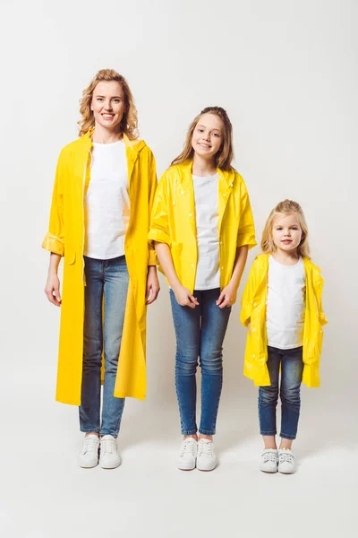 Красива мати і дочки в жовтих плащах на білому — стокове фото