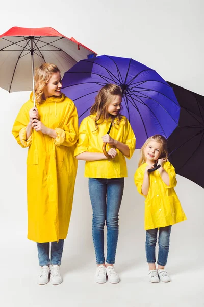 Feliz madre e hijas en impermeables amarillos con paraguas en blanco - foto de stock