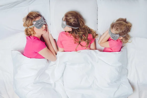 Vista dall'alto di madre e figlie con maschere addormentate a forma di volto di gatto che dormono insieme a letto — Foto stock