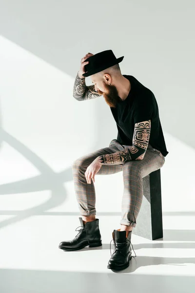 Guapo barbudo tatuado hombre tocando sombrero en blanco - foto de stock