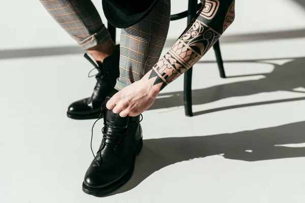 Imagen recortada de hombre tatuado que fija los zapatos - foto de stock