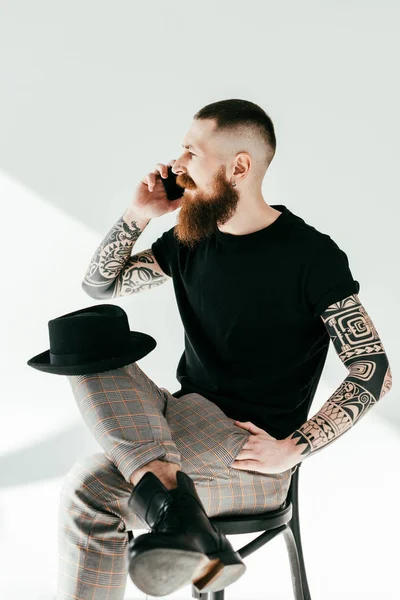 Bonito barbudo tatuado homem falando por smartphone no branco — Fotografia de Stock