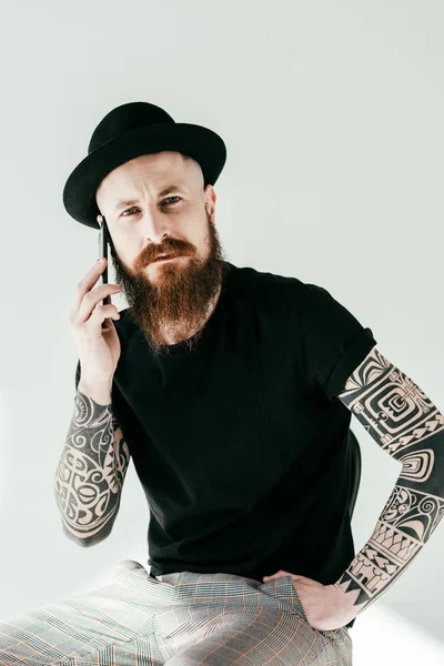 Bearded tattooed man talking by smartphone and looking at camera on white — Stock Photo