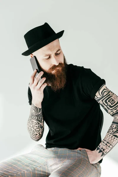 Guapo barbudo tatuado hombre hablando por teléfono inteligente y mirando hacia abajo en blanco - foto de stock