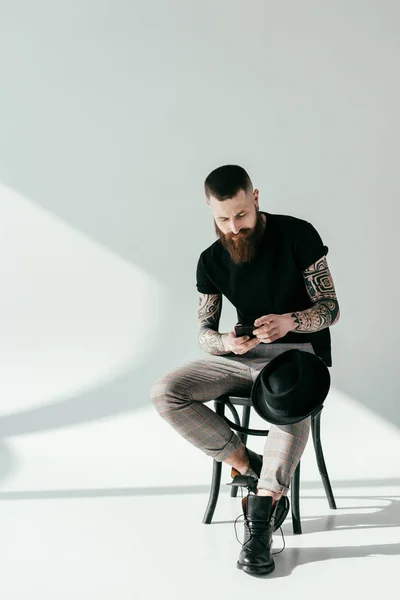Élégant homme tatoué barbu en utilisant smartphone sur blanc — Photo de stock