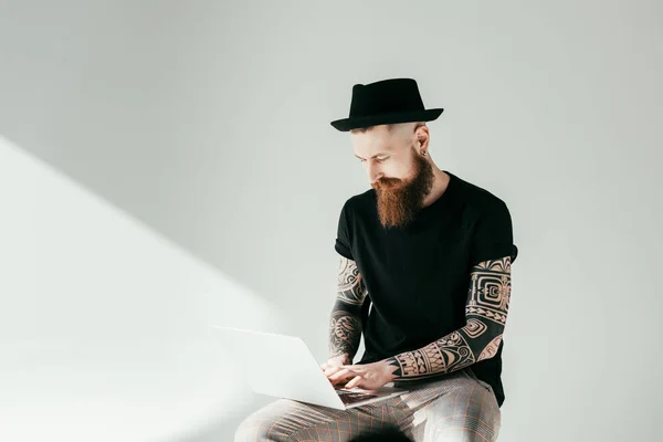 Handsome bearded tattooed man using laptop on white — Stock Photo