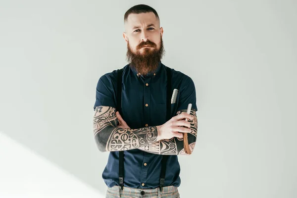 Татуированный мужчина держит бритву и смотрит на камеру, изолированную на белом — стоковое фото