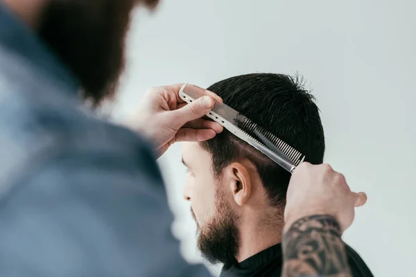 Cropped image of barber cutting customer hair with scissors and comb at barbershop isolated on white — Stock Photo