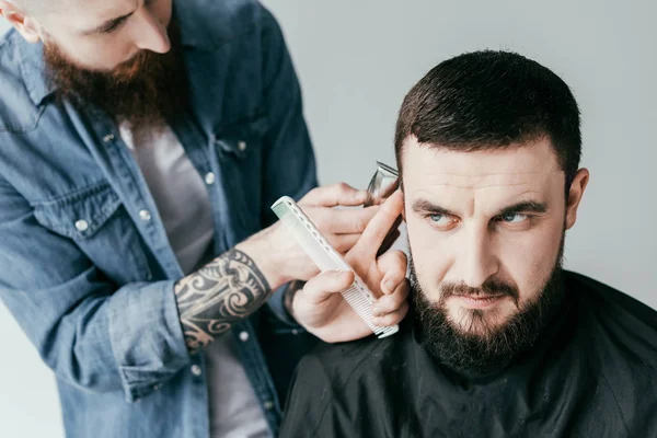 Peluquero afeitar el cabello del cliente con la máquina de afeitar en la barbería aislado en blanco - foto de stock