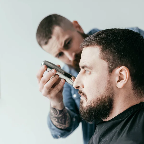 Side view of barber trimming customer beard at barbershop isolated on white — Stock Photo