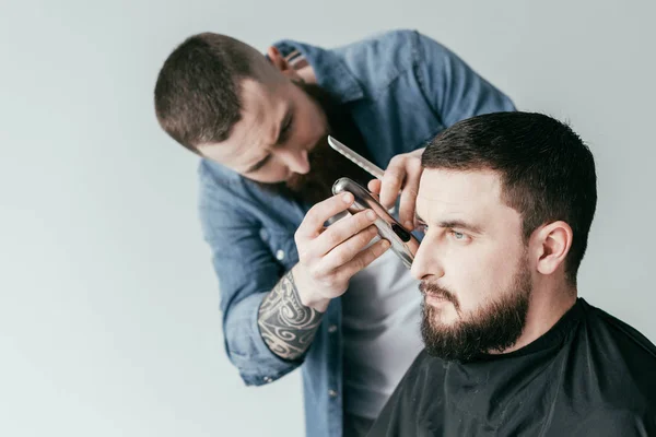 Serious barber trimming customer beard at barbershop isolated on white — Stock Photo