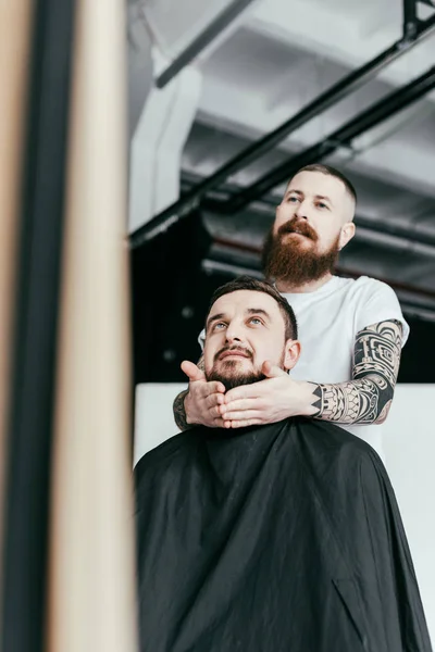 Barber styling customer beard and looking at mirror at barbershop — Stock Photo