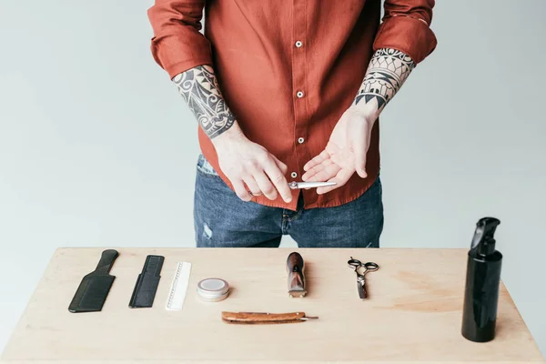 Cropped image of tattooed barber holding scissors above table with equipment isolated on white — Stock Photo
