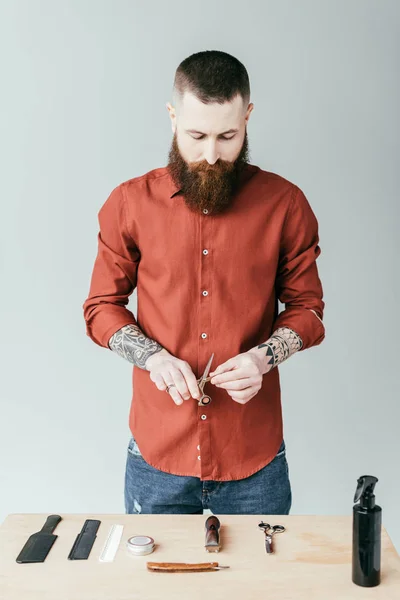Bonito barbeiro segurando tesoura e olhando para o equipamento isolado no branco — Fotografia de Stock