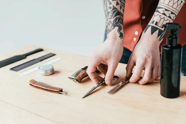 Imagem cortada de barbeiro tatuado colocando equipamentos na mesa isolado em branco — Fotografia de Stock