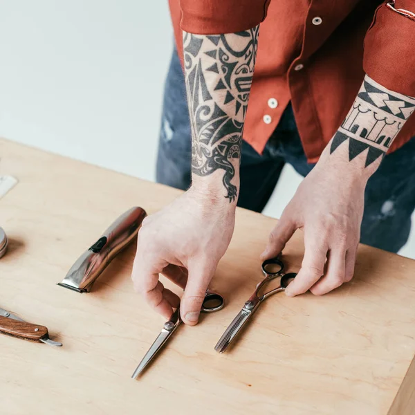 Imagem cortada de barbeiro tatuado tomando tesoura da mesa isolada em branco — Fotografia de Stock