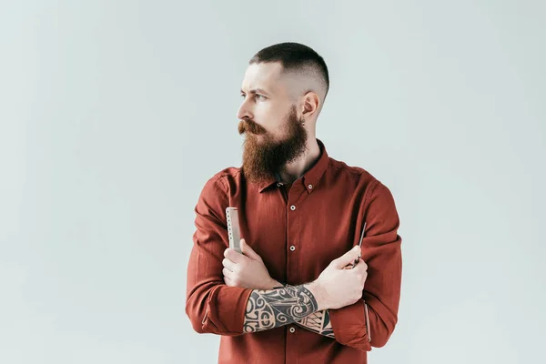 Bearded handsome barber holding comb and scissors in crossed arms isolated on white — Stock Photo